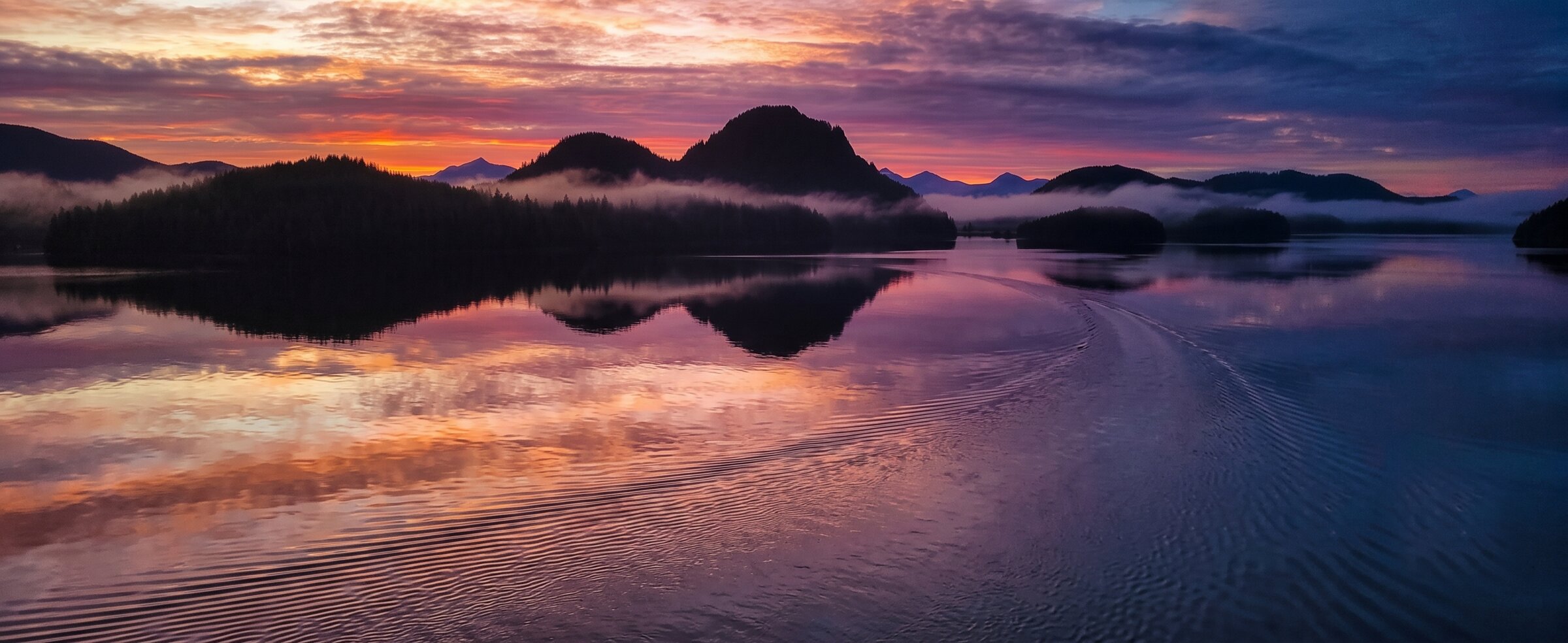 Pink and violet sunset sky mirrored on the ocean — evening boat trip from Tofino harbour